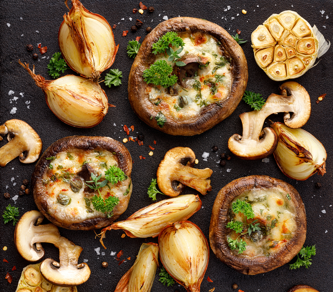 Roasted portobello mushrooms stuffed with cheese and herbs on a black iron  background, top view. Vegetarian meal